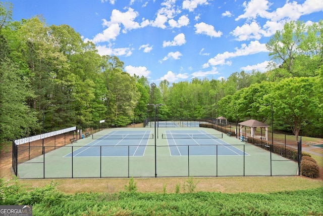 view of tennis court with fence and a view of trees