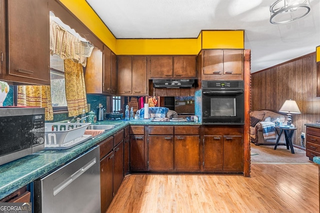 kitchen with light wood-style flooring, dark countertops, appliances with stainless steel finishes, and under cabinet range hood