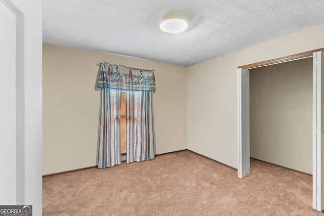 unfurnished bedroom featuring light colored carpet, a textured ceiling, and baseboards