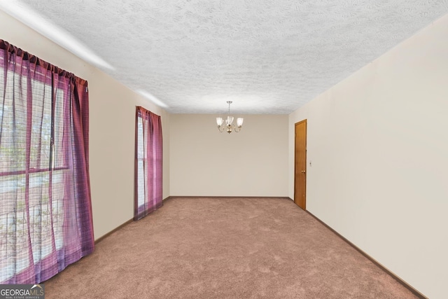 empty room with an inviting chandelier, light colored carpet, and a textured ceiling