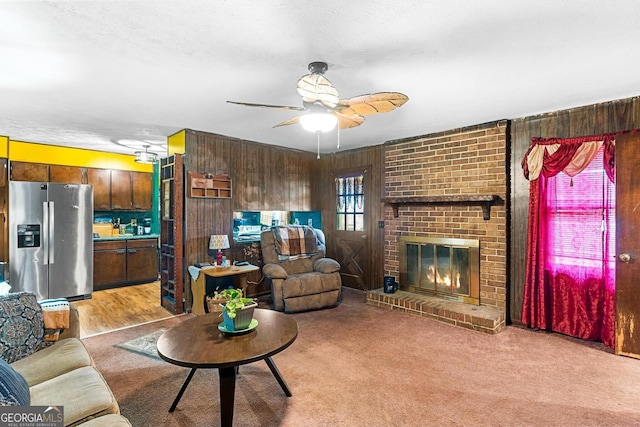 living room featuring wood walls, ceiling fan, light carpet, and a brick fireplace