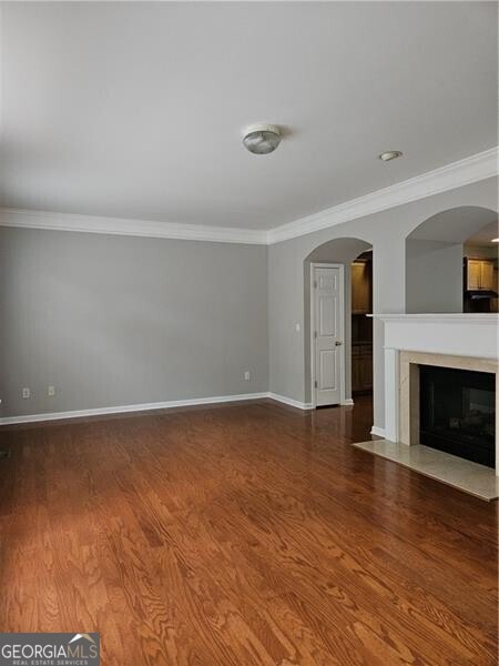 unfurnished living room with baseboards, ornamental molding, and wood finished floors