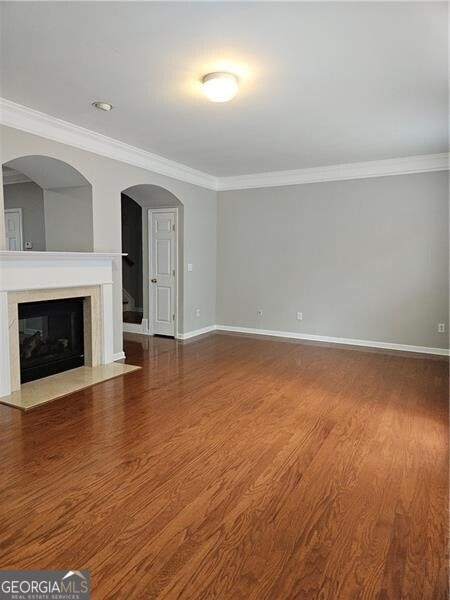 unfurnished living room featuring crown molding, baseboards, and wood finished floors