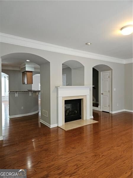 unfurnished living room featuring a high end fireplace, baseboards, ornamental molding, and dark wood-type flooring