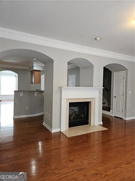 unfurnished living room featuring crown molding, a fireplace, wood finished floors, stairway, and baseboards