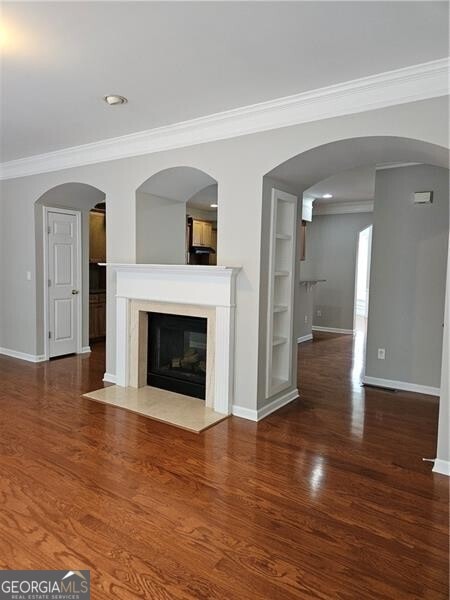 unfurnished living room with crown molding, a fireplace, built in features, baseboards, and wood finished floors