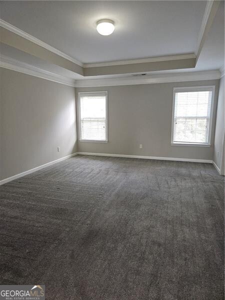 unfurnished room with baseboards, ornamental molding, a raised ceiling, and dark colored carpet