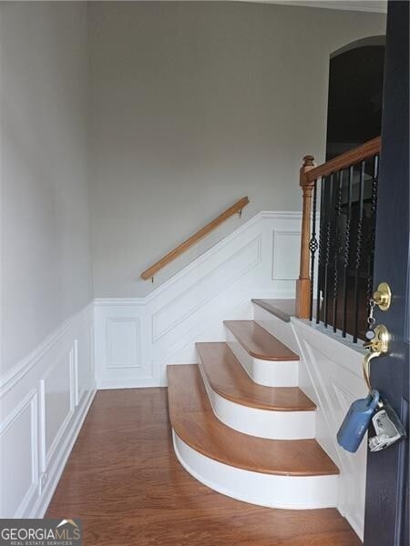 staircase with wood finished floors, a decorative wall, and a wainscoted wall