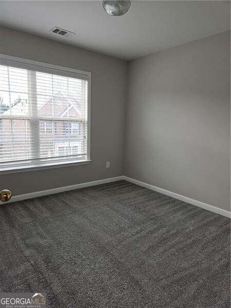 empty room with baseboards, dark carpet, and visible vents
