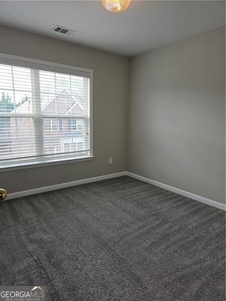 empty room with baseboards, dark carpet, and visible vents