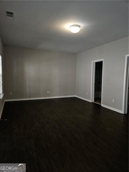 empty room featuring baseboards, dark wood finished floors, and visible vents