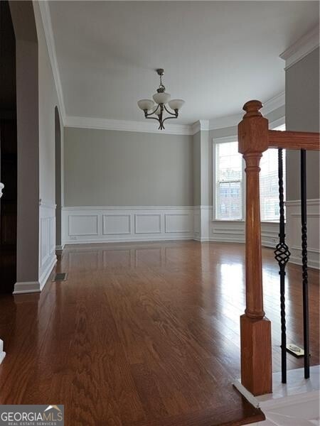 interior space featuring crown molding, wainscoting, wood finished floors, and a chandelier