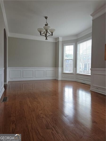 empty room with dark wood-style flooring, arched walkways, an inviting chandelier, and visible vents