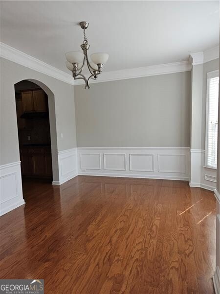 unfurnished dining area with arched walkways, wood finished floors, a notable chandelier, and ornamental molding