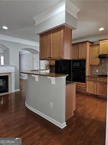 kitchen with crown molding, black appliances, dark stone countertops, a peninsula, and a breakfast bar