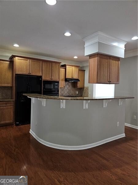 kitchen featuring ornamental molding, a kitchen breakfast bar, brown cabinets, and black appliances