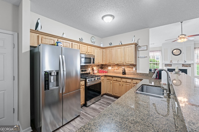 kitchen featuring appliances with stainless steel finishes, stone counters, backsplash, a sink, and light wood-type flooring