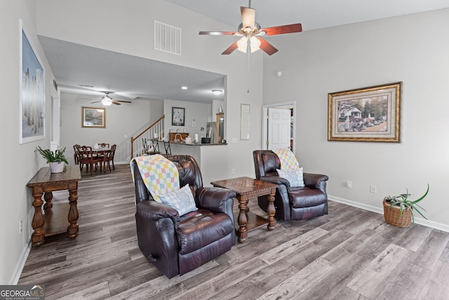 living area featuring wood finished floors, ceiling fan, visible vents, and stairs