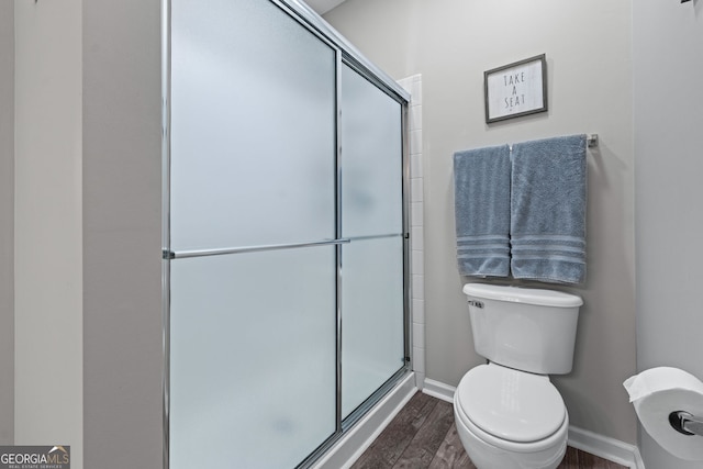 full bathroom with wood finished floors, toilet, a stall shower, and baseboards