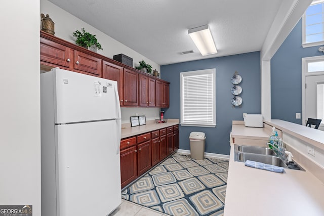 kitchen featuring a sink, reddish brown cabinets, visible vents, light countertops, and freestanding refrigerator