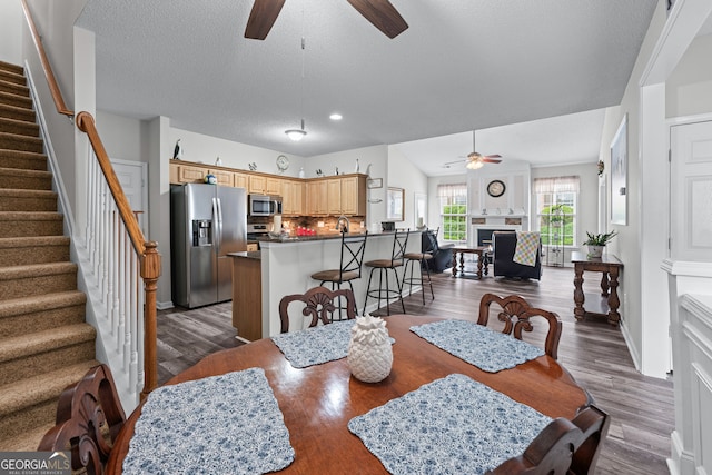 dining area featuring a textured ceiling, ceiling fan, dark wood-type flooring, and stairs