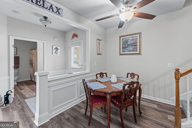 dining area featuring dark wood-style flooring, stairway, a wainscoted wall, a ceiling fan, and a textured ceiling