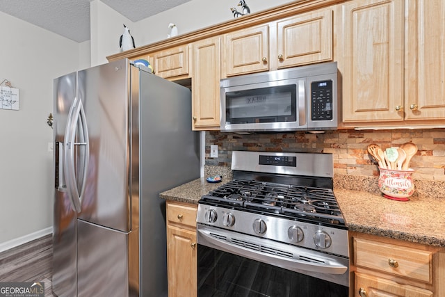kitchen featuring light stone counters, stainless steel appliances, light brown cabinetry, wood finished floors, and backsplash