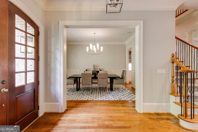 foyer entrance with light wood-style flooring, a chandelier, stairs, crown molding, and wainscoting