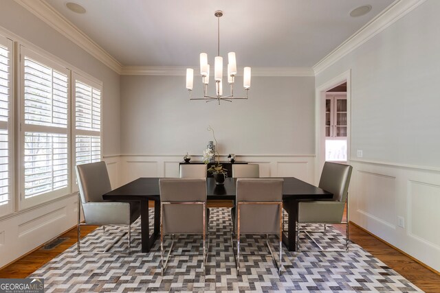 dining space featuring plenty of natural light, a decorative wall, crown molding, a chandelier, and wood finished floors