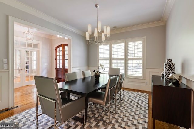 dining room featuring a chandelier, arched walkways, french doors, a decorative wall, and a wainscoted wall