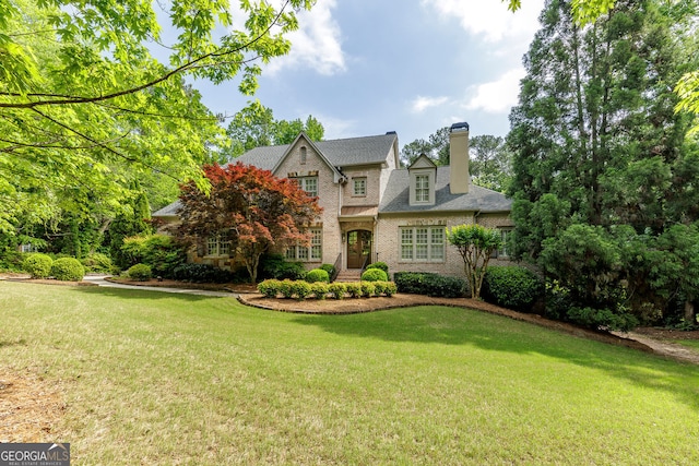 tudor home featuring a chimney, a front lawn, and brick siding