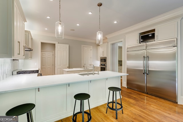 kitchen featuring built in appliances, crown molding, a peninsula, light countertops, and a sink