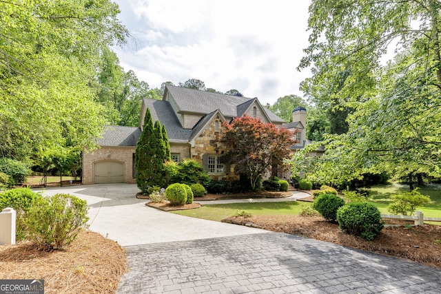 view of front of house with decorative driveway, an attached garage, stone siding, and roof with shingles