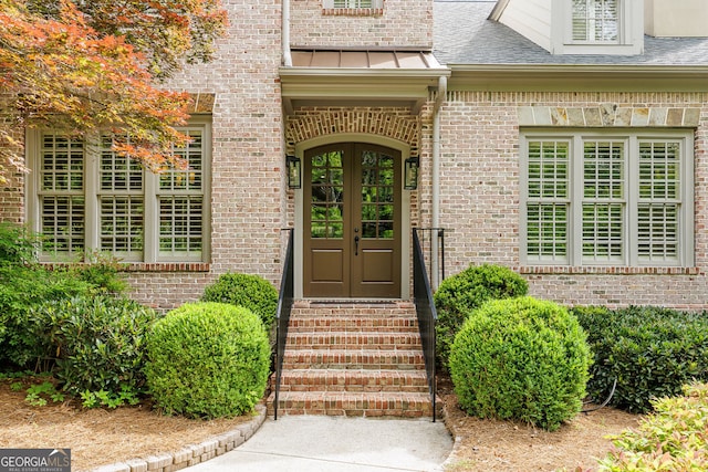 view of exterior entry featuring french doors, brick siding, and a shingled roof
