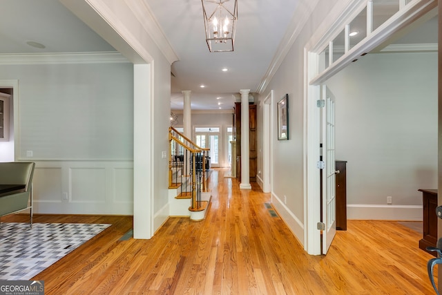 entrance foyer featuring decorative columns, crown molding, light wood finished floors, stairway, and a wainscoted wall