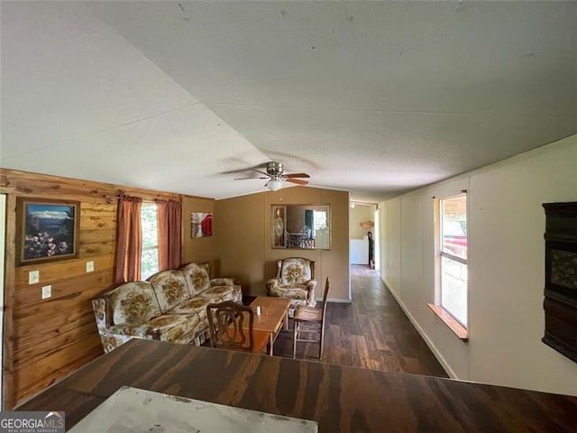 living room featuring wood walls, baseboards, vaulted ceiling, wood finished floors, and a ceiling fan