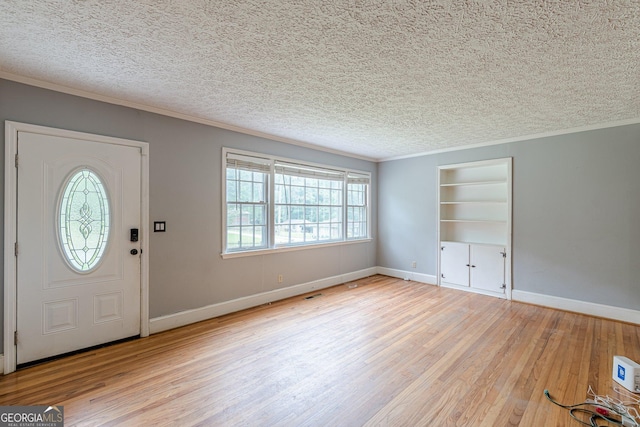 foyer featuring baseboards, a textured ceiling, ornamental molding, and wood finished floors