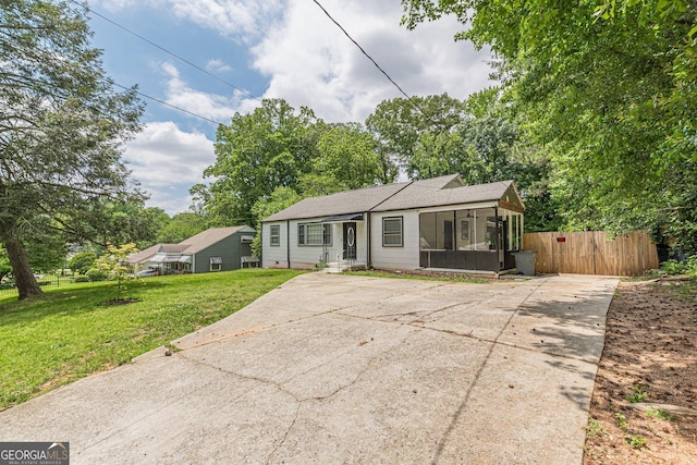 view of front facade featuring a sunroom, a front lawn, fence, and concrete driveway