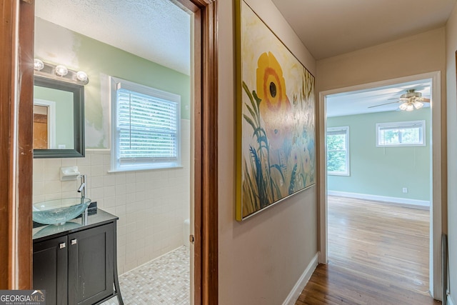 corridor featuring baseboards, tile walls, a sink, and wood finished floors