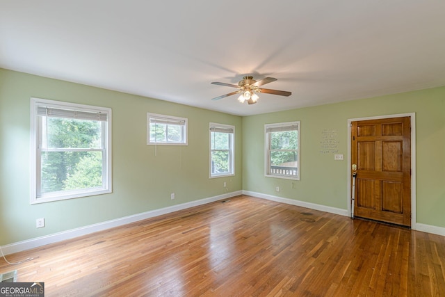 empty room with a ceiling fan, baseboards, plenty of natural light, and wood finished floors