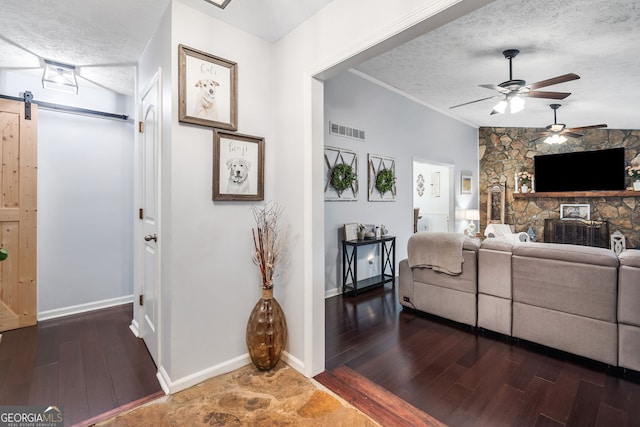 living room featuring a ceiling fan, a textured ceiling, visible vents, and a barn door