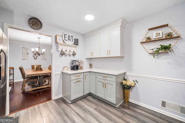 bar featuring an inviting chandelier, baseboards, light wood finished floors, and visible vents