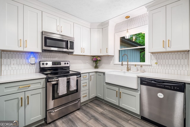 kitchen with dark wood-style flooring, appliances with stainless steel finishes, a sink, light countertops, and backsplash