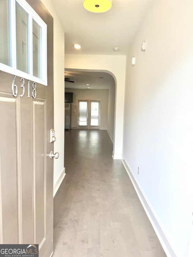 hallway featuring baseboards, arched walkways, and wood finished floors