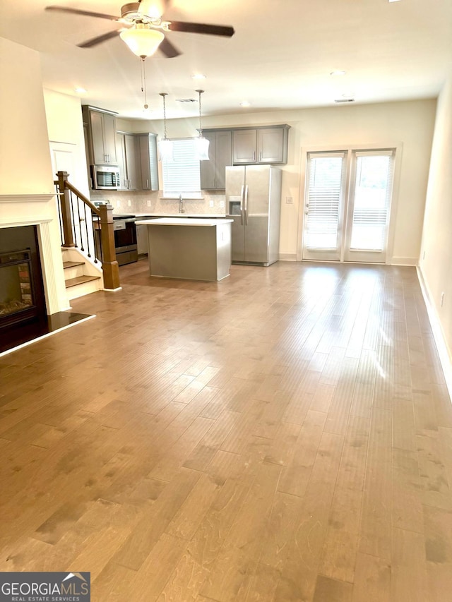 unfurnished living room with a ceiling fan, wood finished floors, a sink, baseboards, and stairs