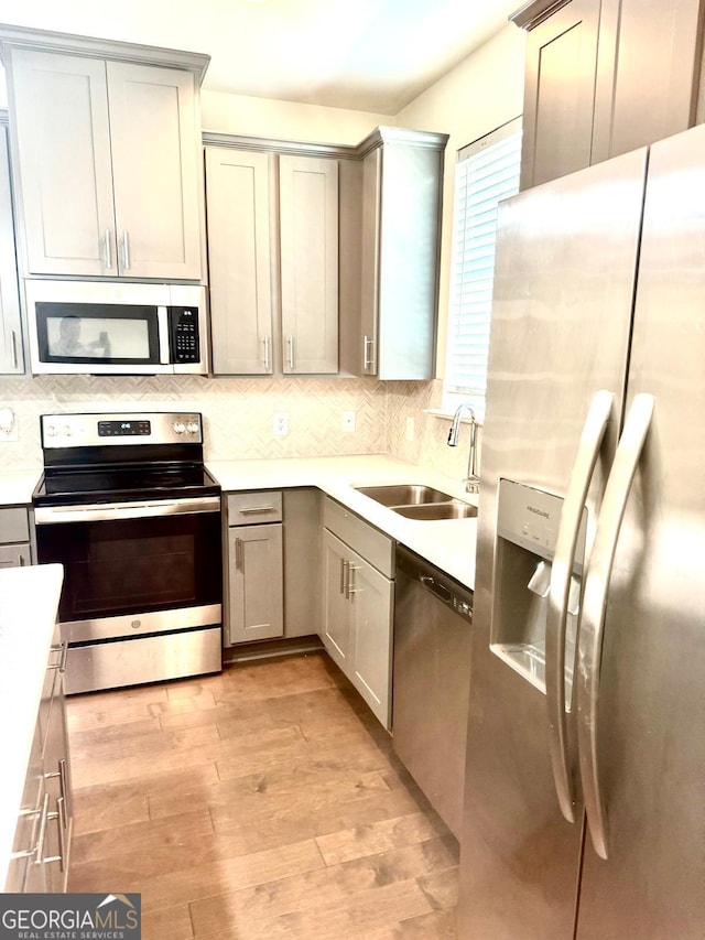 kitchen with appliances with stainless steel finishes, a sink, light countertops, decorative backsplash, and light wood-type flooring