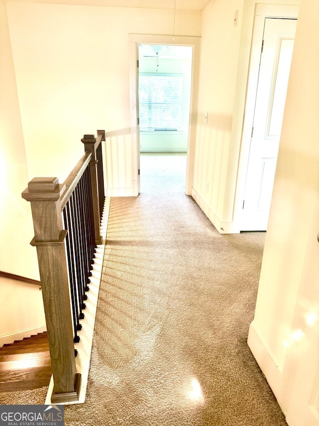 hallway featuring baseboards, an upstairs landing, and carpet