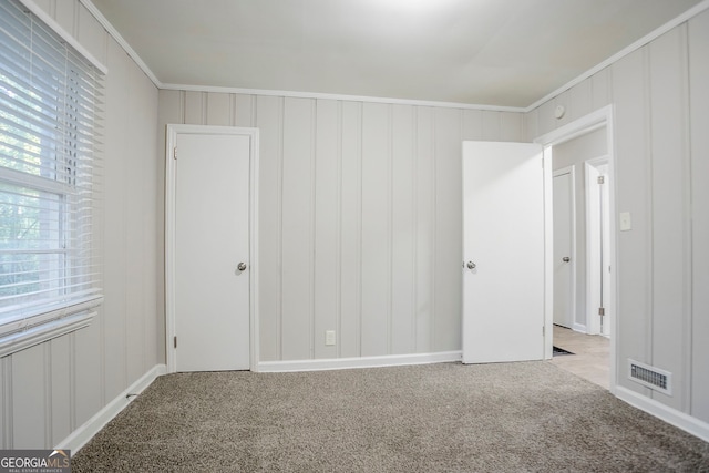 carpeted empty room with baseboards, visible vents, ornamental molding, and a decorative wall