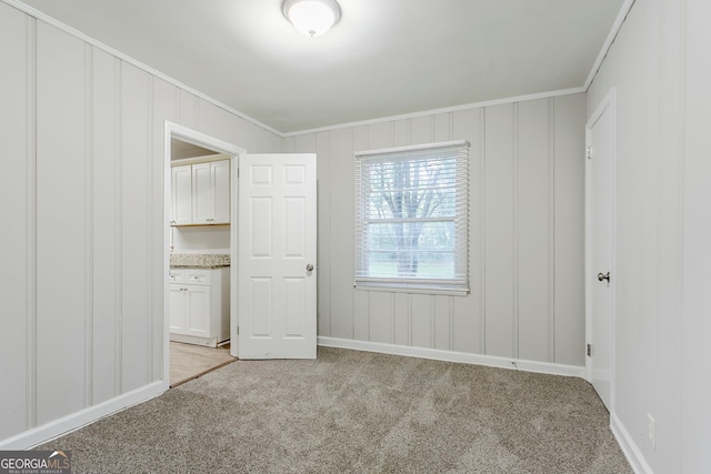unfurnished bedroom with a decorative wall, crown molding, baseboards, and light carpet