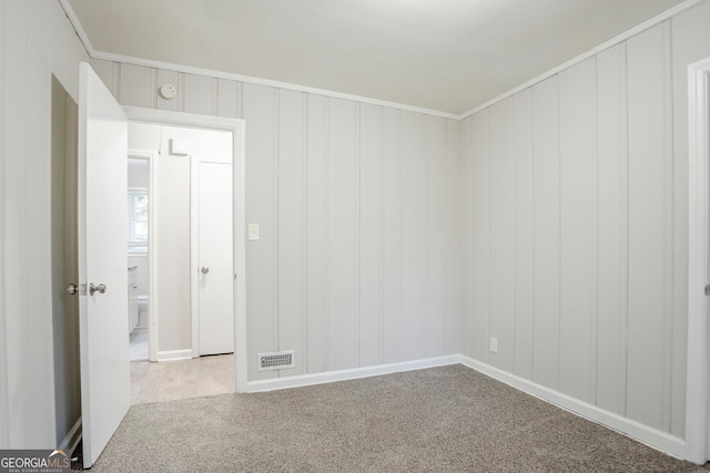 empty room featuring a decorative wall, ornamental molding, carpet flooring, baseboards, and visible vents